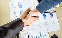 Image of two businesspeople shaking hands over charts and graphs.