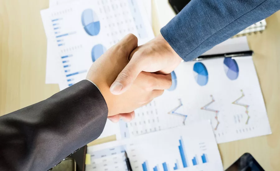 Image of two businesspeople shaking hands over charts and graphs.