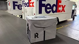 Image of reusable FedEx box with FedEx trucks in the background.