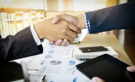 Image of two businesspeople shaking hands over charts and graphs.
