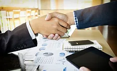 Image of two businesspeople shaking hands over charts and graphs.