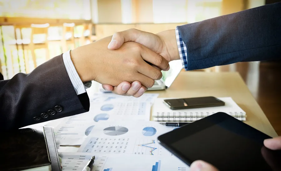 Image of two businesspeople shaking hands over charts and graphs.
