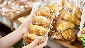 Image of a person picking up croissants packed in flexible packaging at a supermarket.