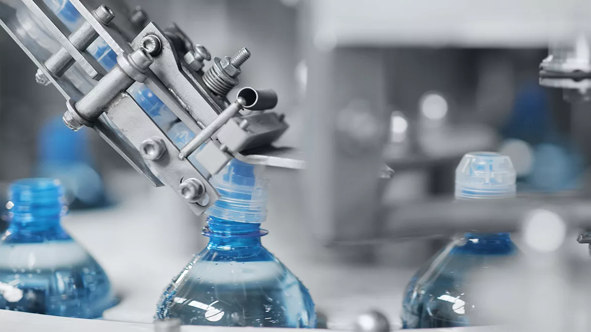 Machinery putting caps on blue water bottles.