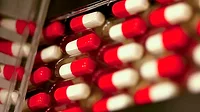 Pharmaceutical machinery placing red and white capsules inside blister packaging on a conveyor blet.